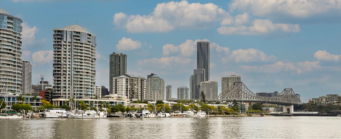 Young Australian first home buyer reviewing Brisbane property listings stamp duty QLD grant documents on laptop with city skyline