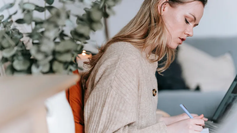 Person taking notes beside a laptop at home while checking annual take-home pay figures